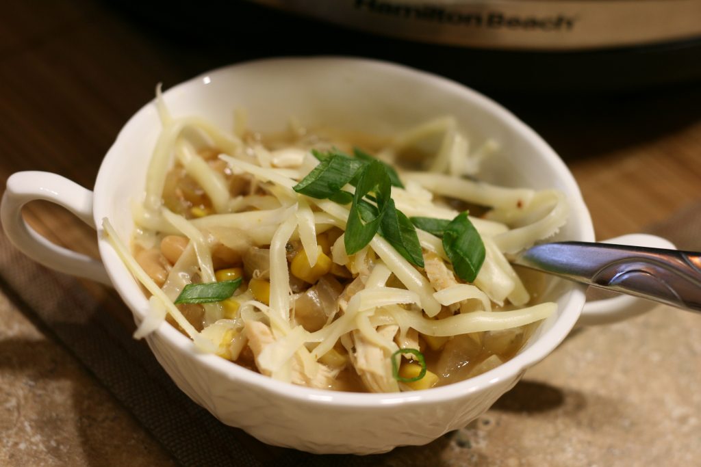 Slow cooker white chili in a bowl with cheese on top