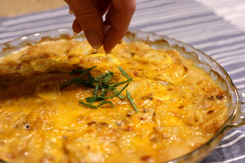 sprinkling basil on top of potato and yellow squash au gratin